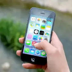 Dłoń trzyma smartfon z widocznym ekranem głównym i ikonami aplikacji.