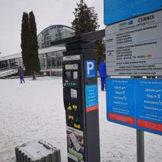 Parkomat APCOA FLOW w zimowej scenerii, obok cennik parkingu.