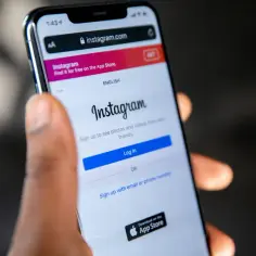 Dłoń trzyma smartfon z otwartą stroną logowania Instagram.com. Zastanawiasz się, jak pobrać film z Instagrama?