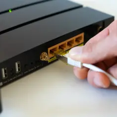 Dłoń podłącza kabel sieciowy do routera. Widoczny przycisk RESET, który może pomóc, gdy zastanawiasz się, jak zresetować router.