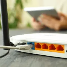 Router z podłączonym kablem LAN. W tle osoba korzystająca z tabletu, co pokazuje, wlan co to jest - bezprzewodowy dostęp do internetu.