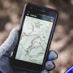 Ręka w rękawiczce trzyma telefon z aplikacją na rower Trailforks, pokazującą mapę szlaków w Beskidzie Małym.