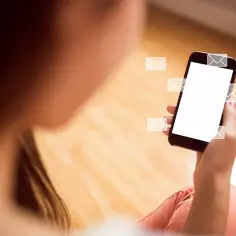 Osoba trzymająca smartfon z ikonami wiadomości wychodzących z ekranu.