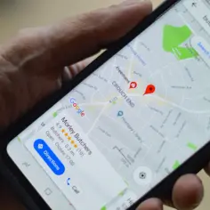 Dłoń trzyma smartfon z mapą Google. Widoczne są google maps współrzędne i wyszukiwanie "butcher".