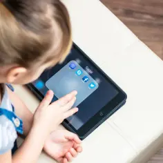 Dziecko dotyka ekranu tabletu z ikonami aplikacji społecznościowych, w tym Facebooka. Zastanawiam się, od ilu lat jest Facebook i czy to już dla niego?