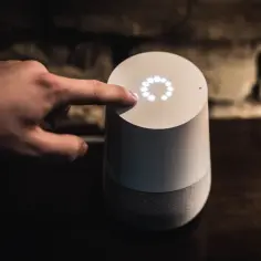 Dłoń dotyka głośnika Google Home, który po polsku odpowiada na pytania.