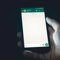 Dłoń trzyma smartfon z otwartym czatem WhatsApp. Widoczny pasek z nazwą kontaktu "Christian" i ikonami. Zastanawiasz się, jak zrobic ankiete na WhatsApp?