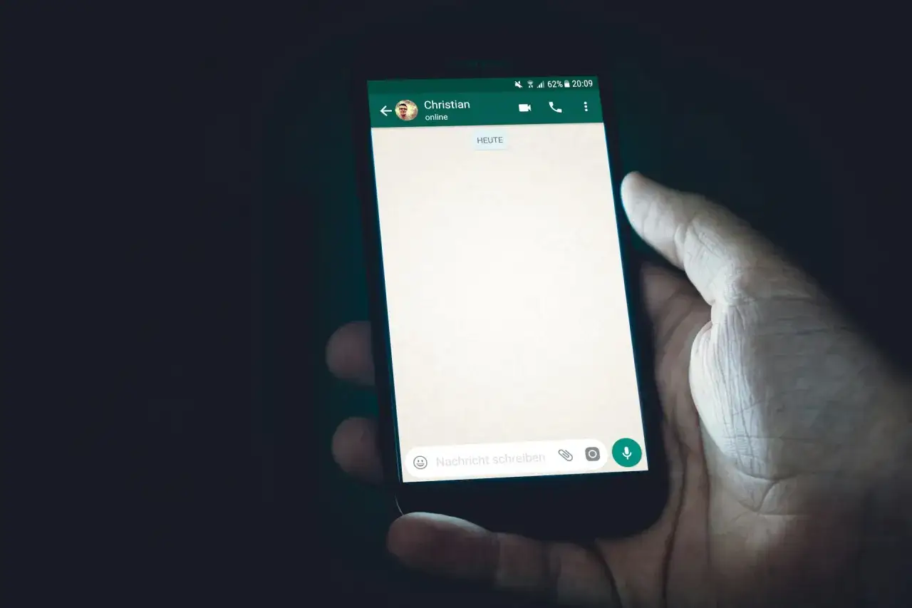 Dłoń trzyma smartfon z otwartym czatem WhatsApp. Zastanawiasz się, jak zrobic ankiete na WhatsApp?