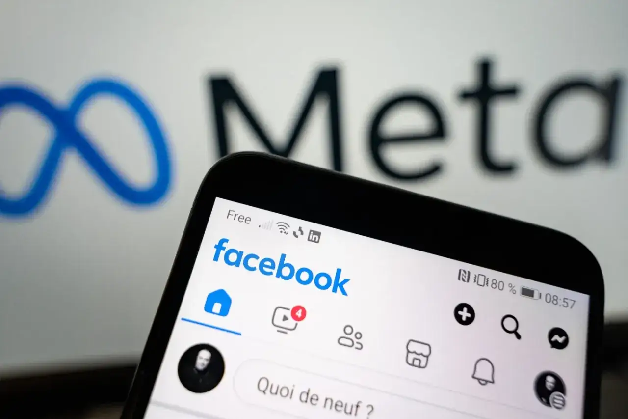 Telefon z aplikacją Facebook na tle logo Meta. Zastanawiasz się, od ilu lat jest Facebook?