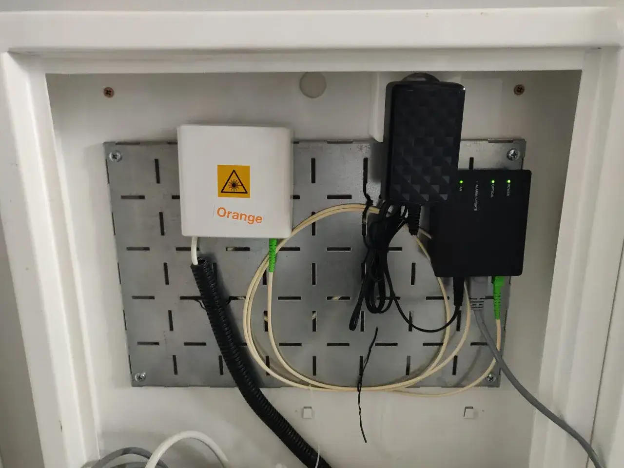 Urządzenie Orange z symbolem lasera, zasilacz i router światłowodowy. To część infrastruktury telekomunikacja polska.