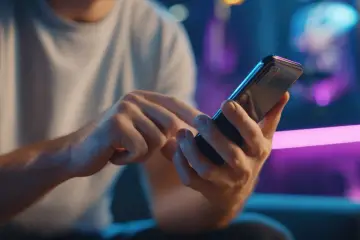 Dłonie trzymające smartfon, w tle neonowe światła. Zastanawiasz się, jak sprawdzić czy telefon jest na podsłuchu?
